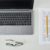 Flat lay of a laptop, exam sheet, and pencil on a white desk, perfect for education and technology themes.