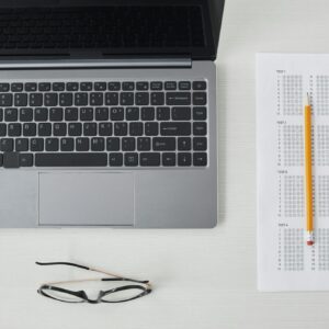 Flat lay of a laptop, exam sheet, and pencil on a white desk, perfect for education and technology themes.
